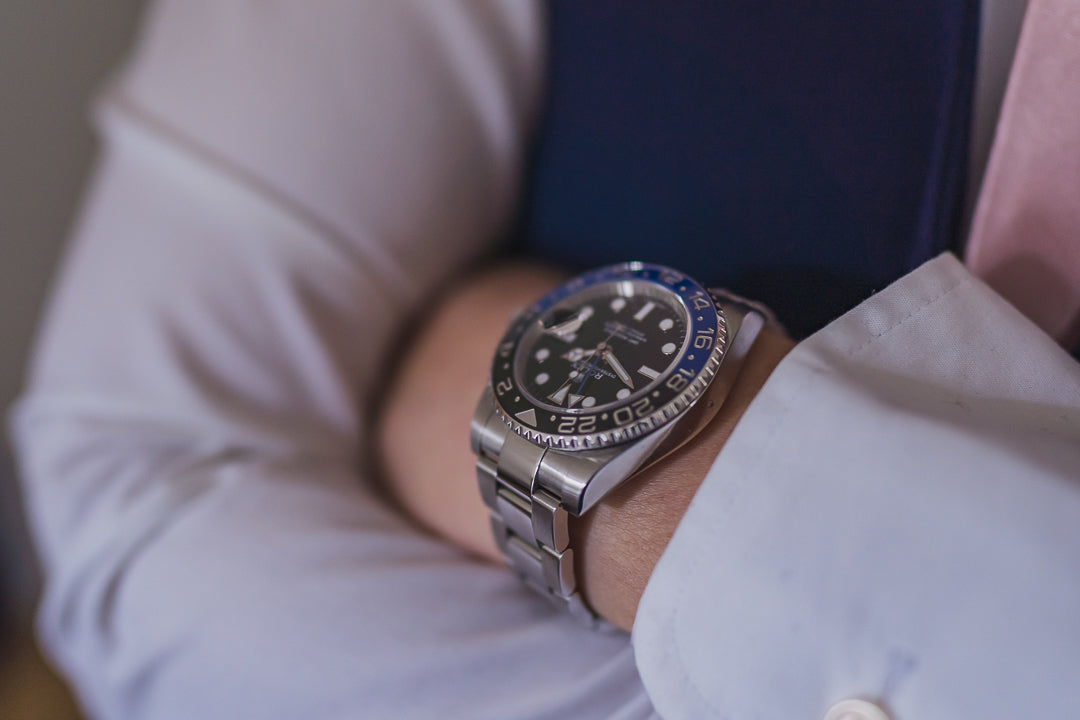 Close-up of a luxury stainless steel watch with black and blue bezel on a man’s wrist, dressed in formal white shirt – premium men’s fashion accessory"
