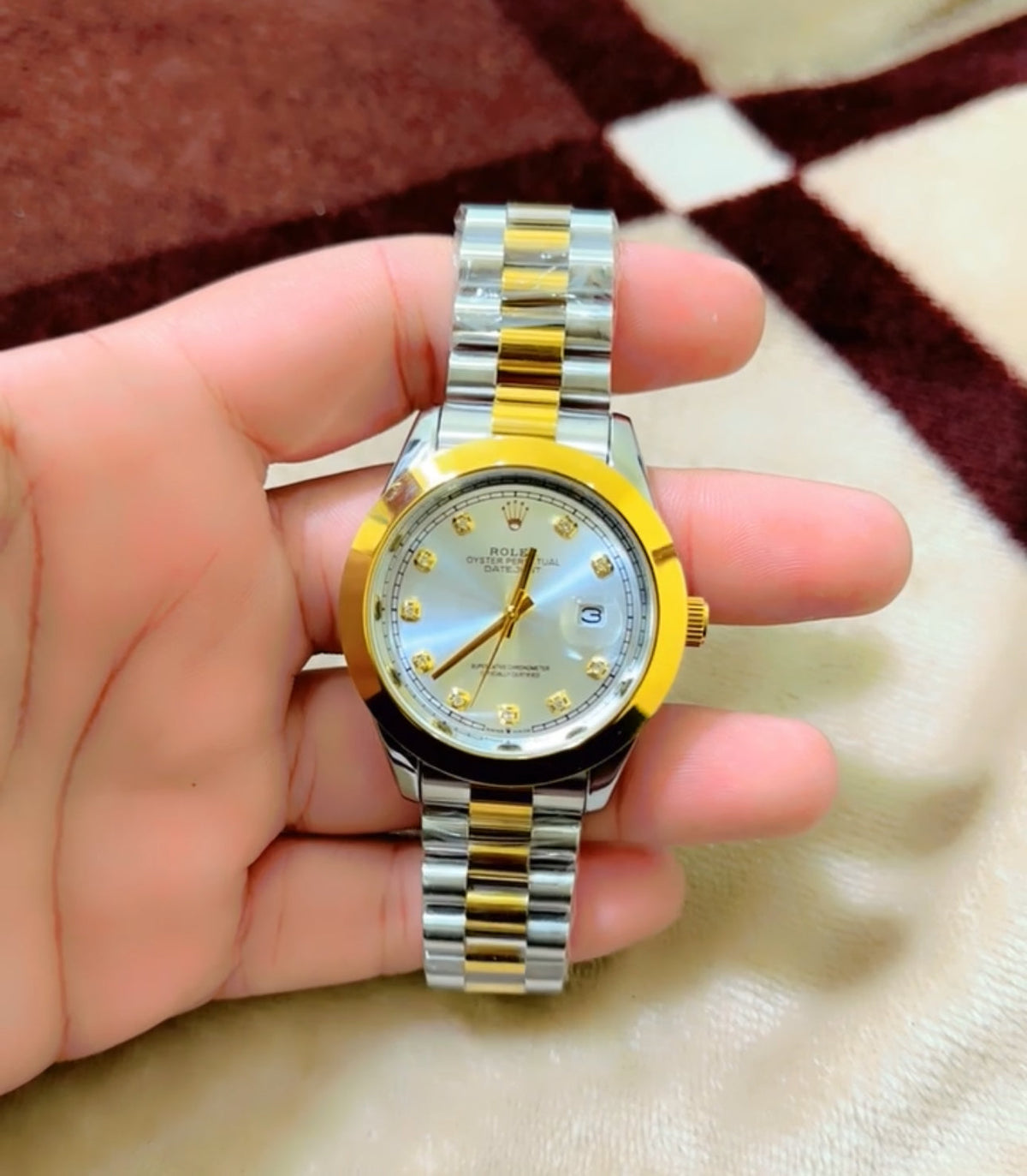 Two-tone watch with gold and silver straps held in a hand on a patterned fabric background